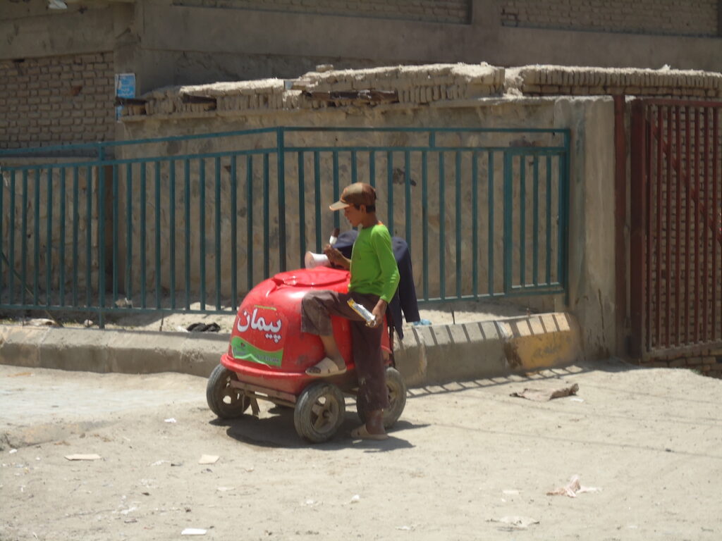 Boy in Kabul standing next to a red ice cream cart