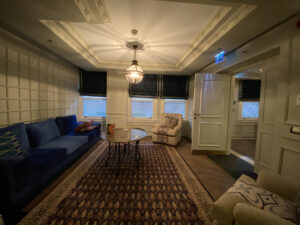 Living room with a blue couch, two white chairs and a table over a Turkish rug