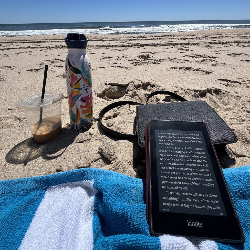 Kindle paperwhite on a beach towel, propped on top of a purse. Waves crashing in the background