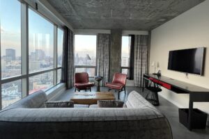 50 bowery suite living room with grey couch, red chairs and large windows overlooking manhattan